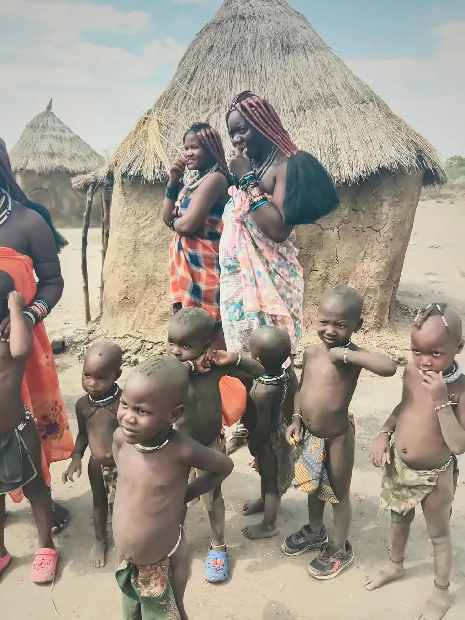Women and young children of the community standing outside their thatched homes in Namibia